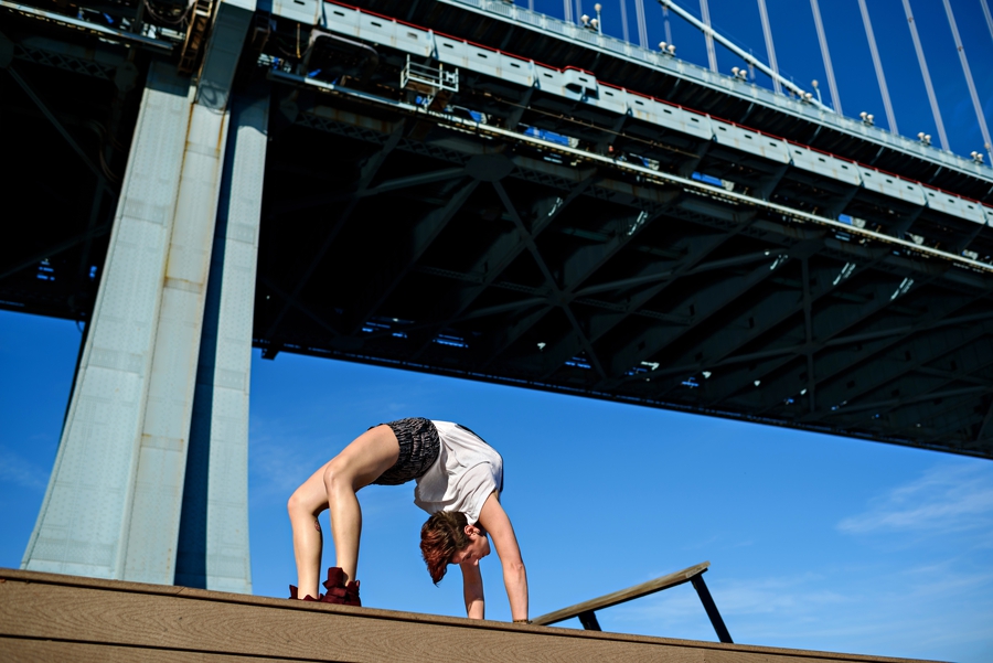 A woman doing a yoga pose under the ben franklin bridge in philly.